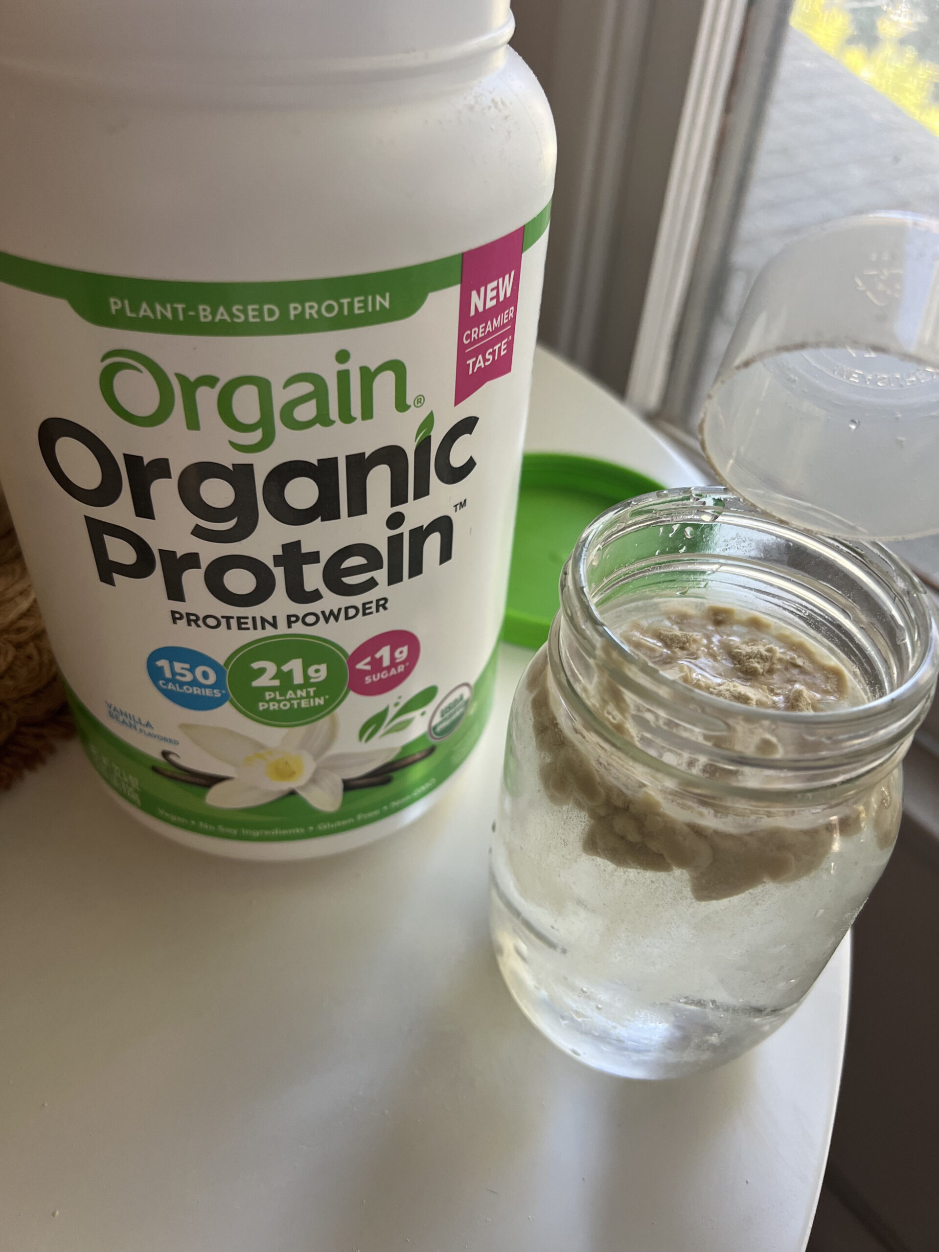 A jar of liquid sits next to a container of Orgain Organic Protein powder on a table.