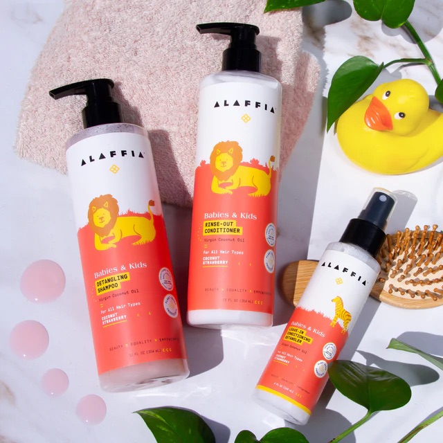 Three baby bath products with lion illustrations on the labels are arranged with a rubber duck, towel, and green leaves.