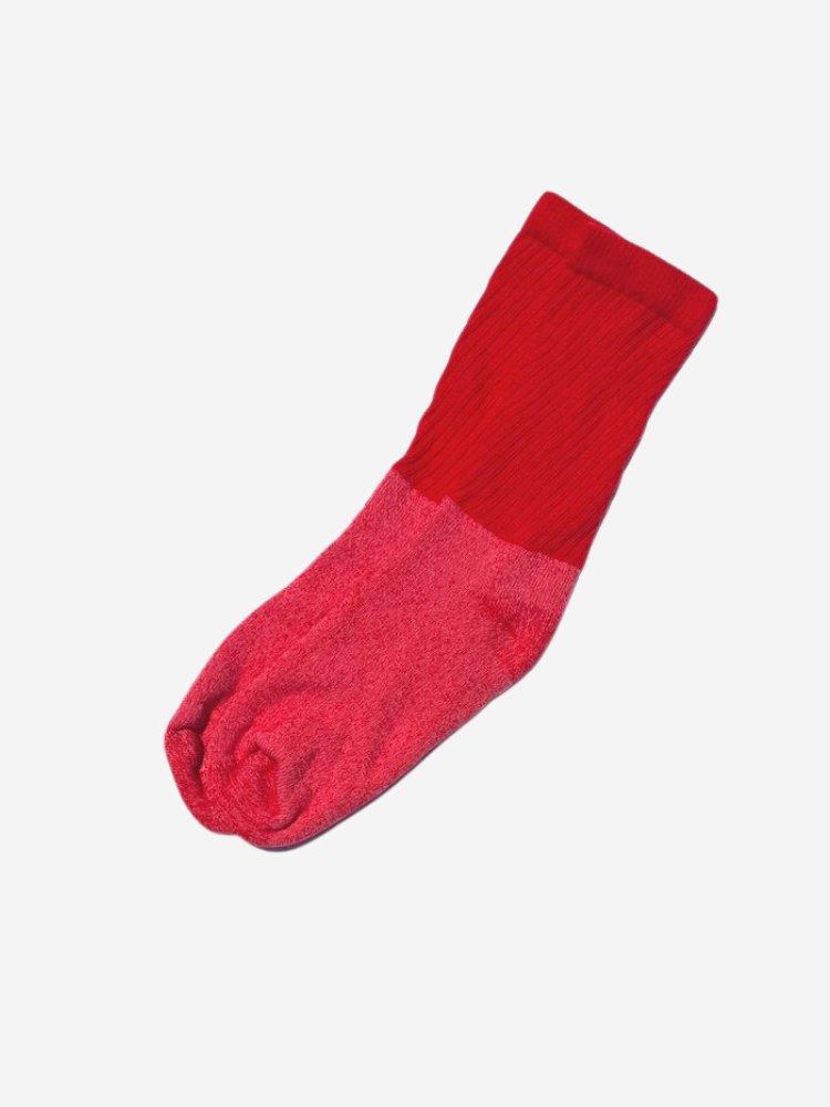 An organic sock with a striking red and pink divided color pattern rests on a pristine white background, showcasing its unique charm.