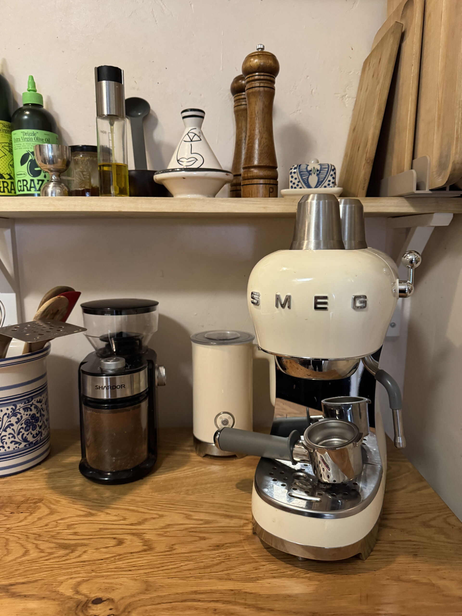 A kitchen counter with a Smeg espresso machine, coffee grinder, and various spices and utensils on a shelf above.