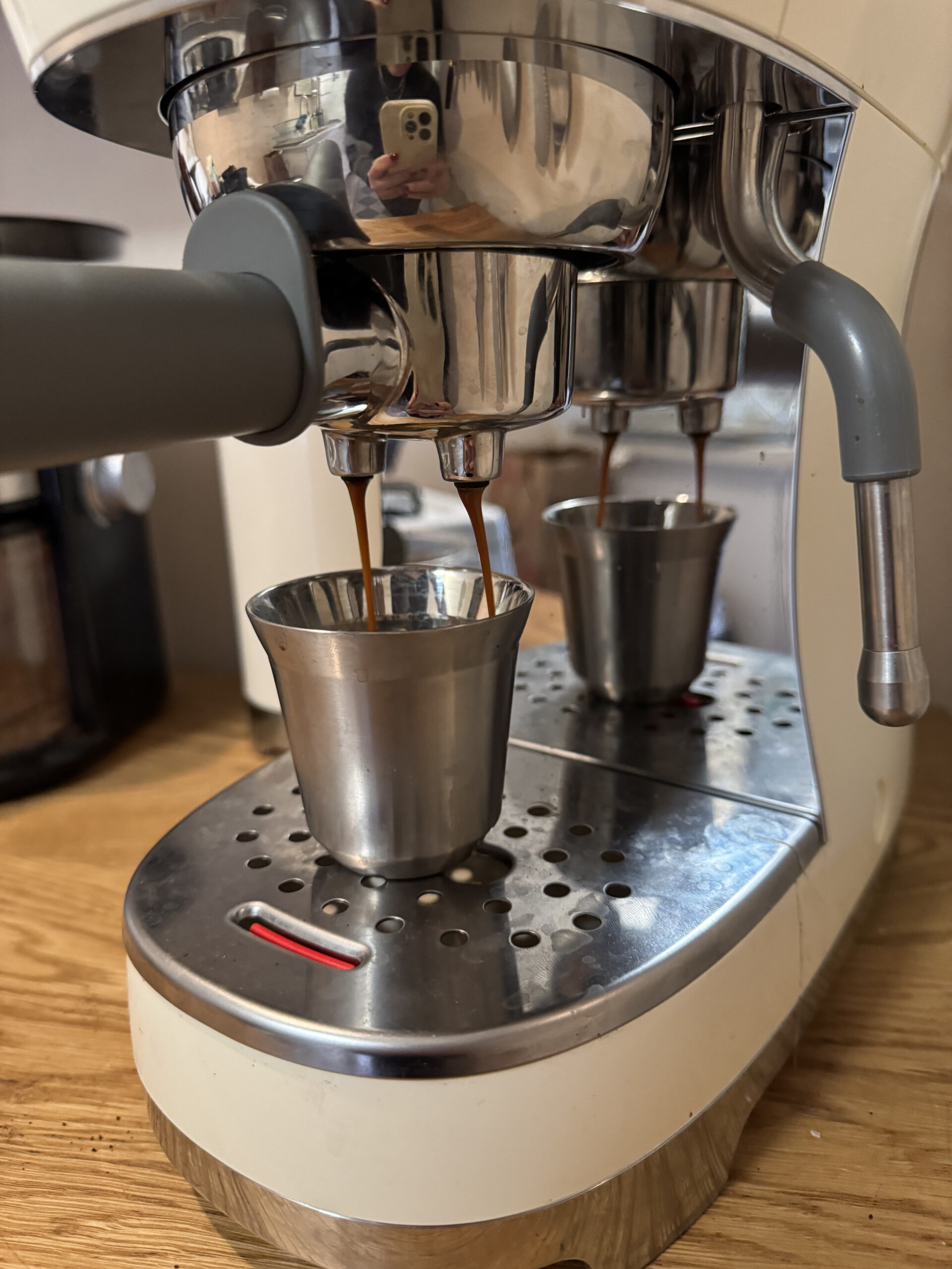 Espresso machine brewing coffee into two metal cups on a wooden countertop.