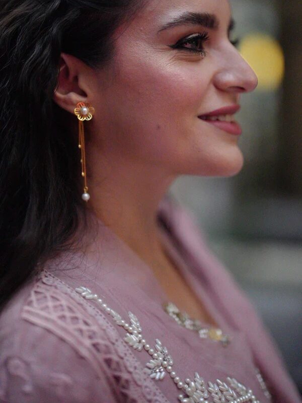 Side profile of a woman with long, dark hair wearing a gold earring and a light pink embroidered top.