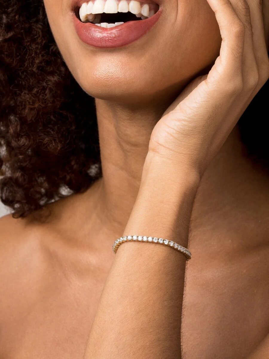 A person with curly hair smiles, wearing a diamond bracelet on their wrist.