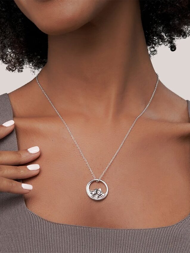 A person wearing a silver necklace with a bird-shaped pendant, shown against a neutral background.