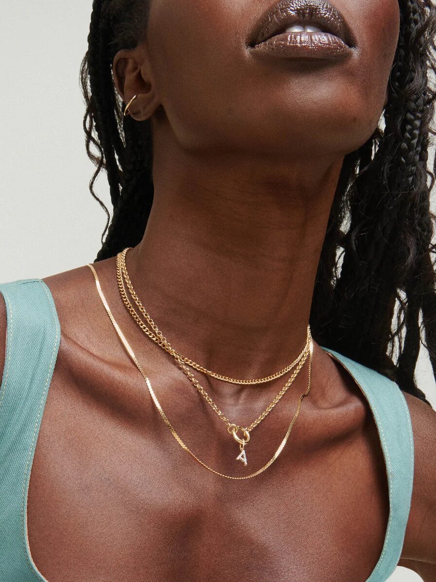 Person wearing layered gold necklaces and a teal sleeveless top, with focus on the jewelry.