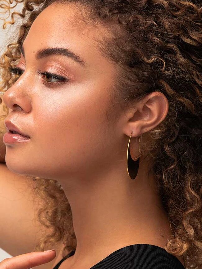 Profile of a person with curly hair wearing a black top and gold hoop earrings.