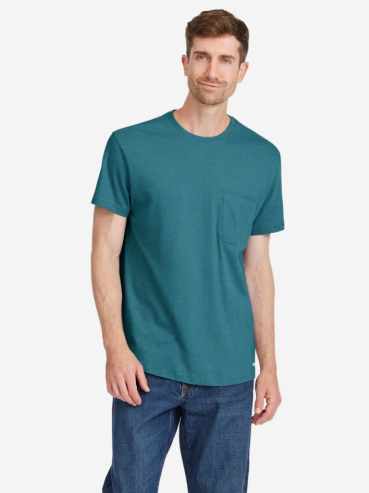 Man wearing a teal t-shirt with a pocket and blue jeans standing against a white background.