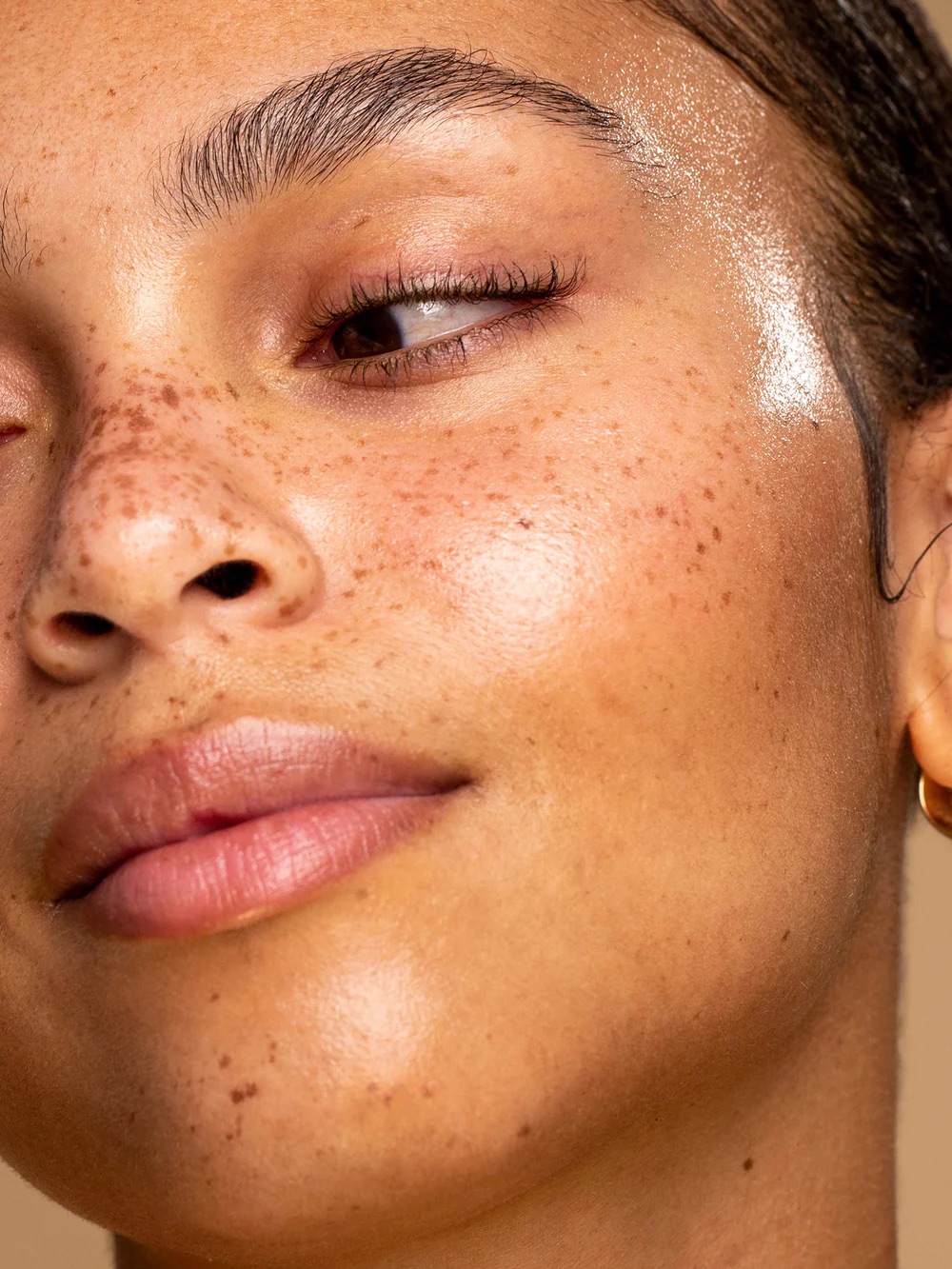 Close-up of a person with freckles on their face, showcasing smooth, dewy skin and natural makeup.