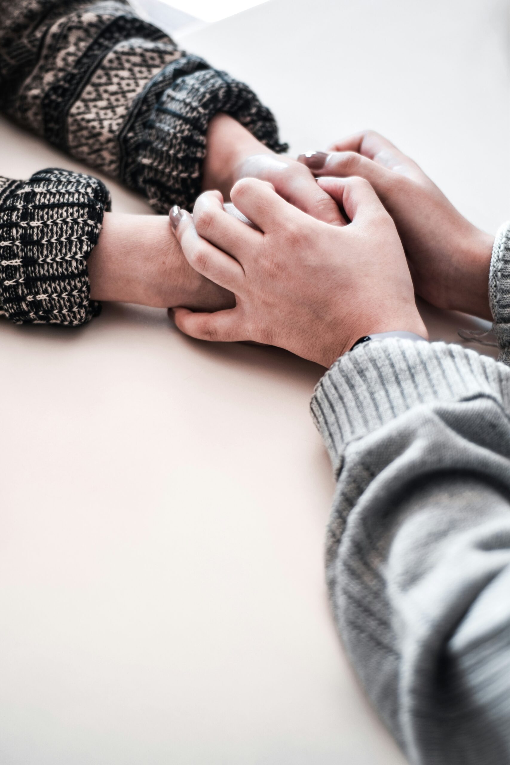 Two people sit at a table and hold hands, each wearing knit sweaters.