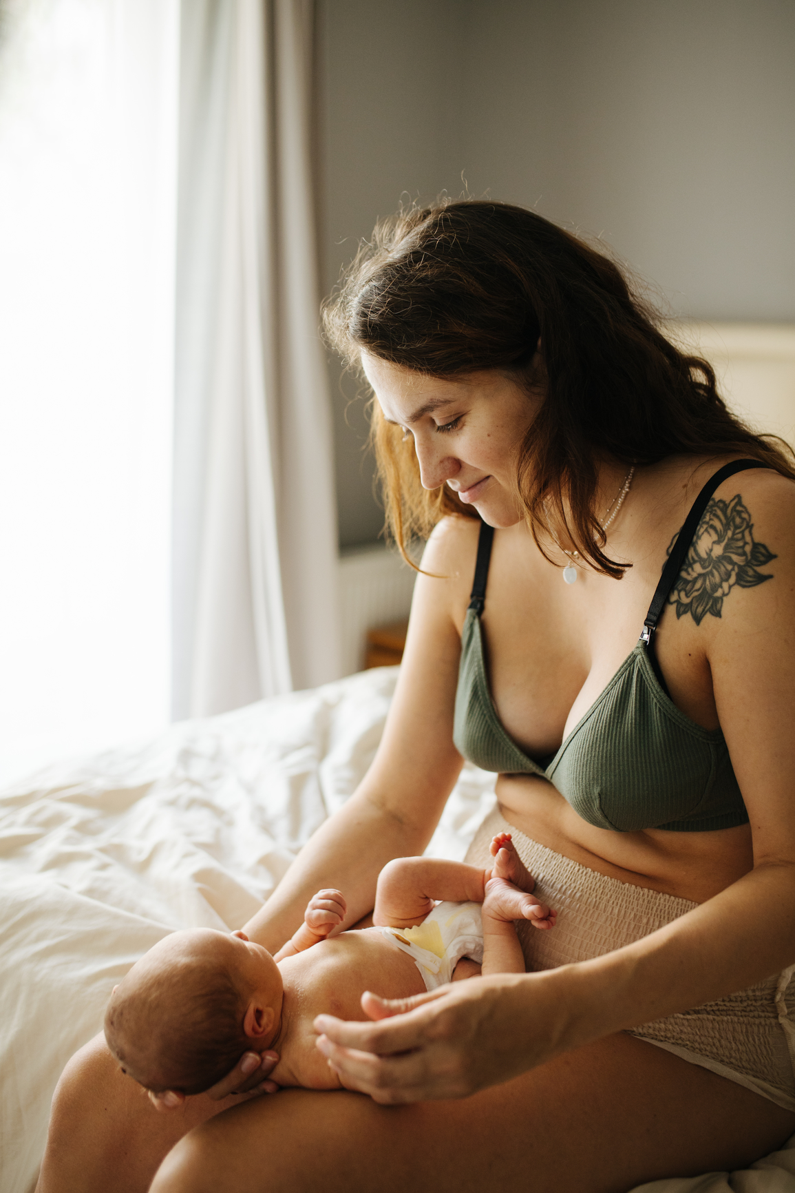 A woman in a green bra sits on a bed, holding a baby on her lap.