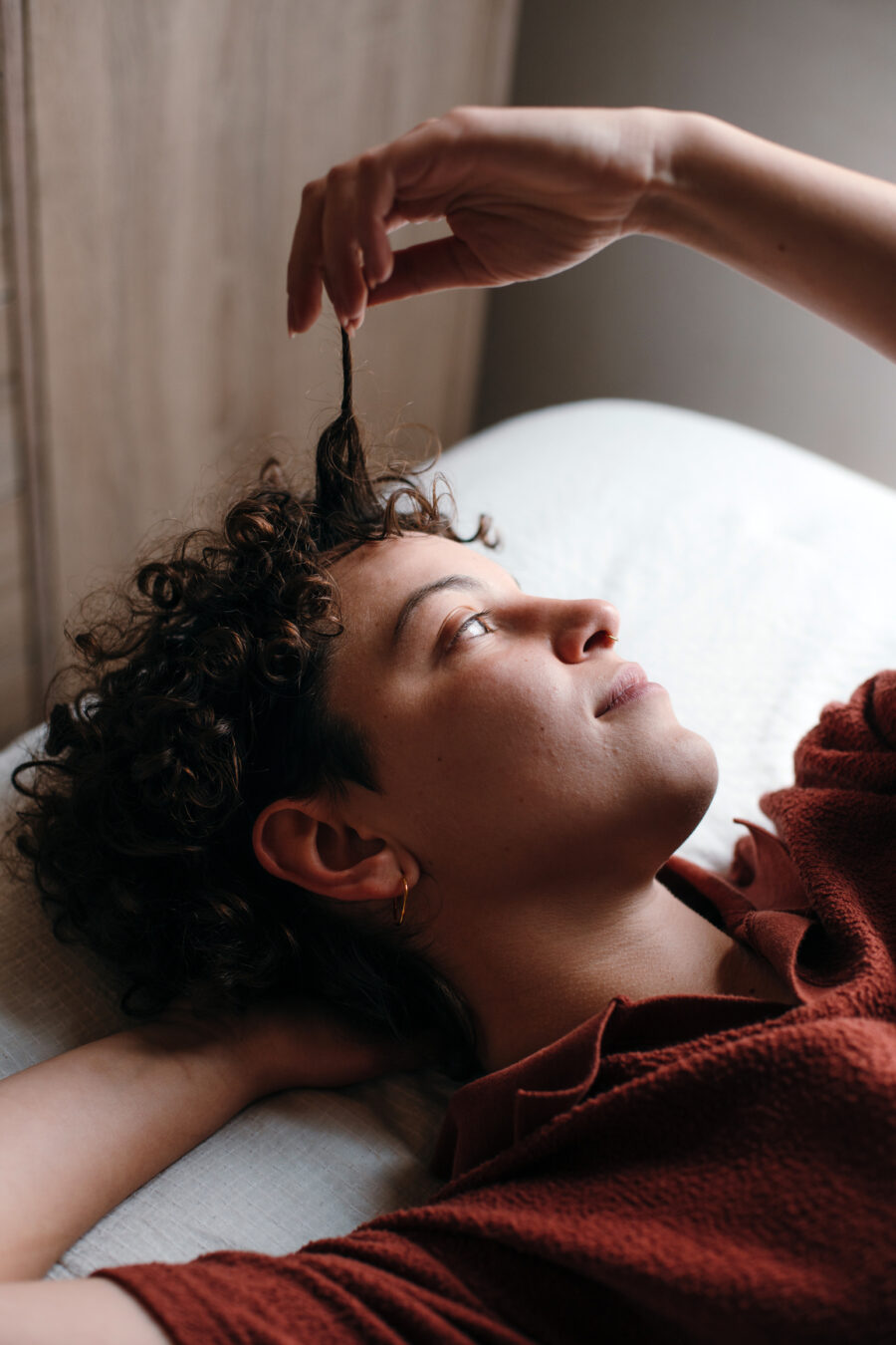 Person lying down, looking up, and gently pulling a curl of their hair with one hand.