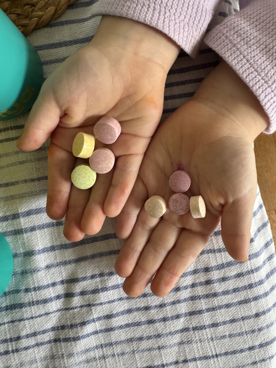 Child's hands holding colorful round tablets on a striped cloth background.