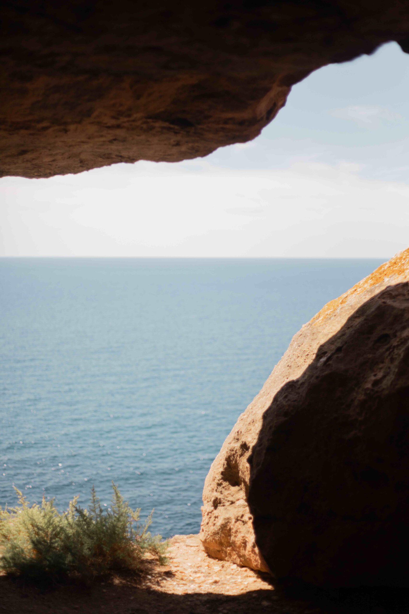 View of the ocean from inside a cave, framed by rocky walls, with a glimpse of bushes at the bottom.