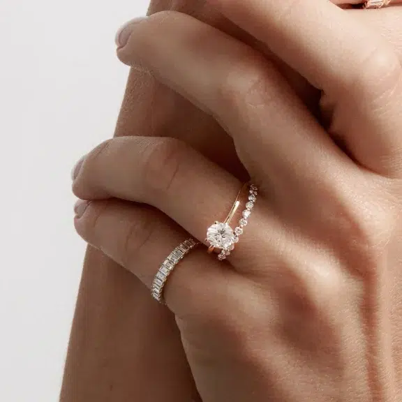 A hand wearing three rings with a diamond solitaire and two bands featuring smaller stones.