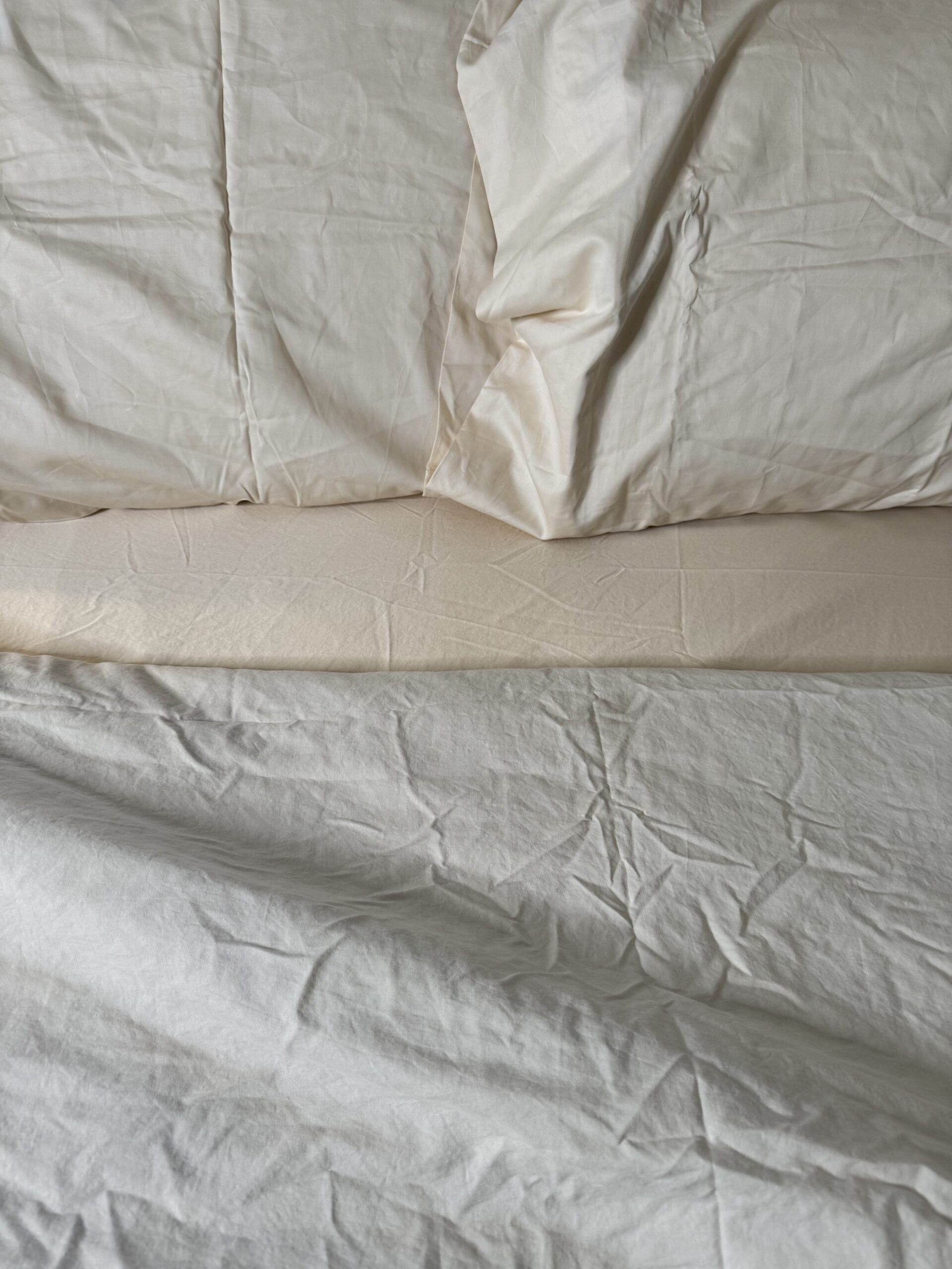 A bed with wrinkled white sheets and pillows on an unmade mattress.