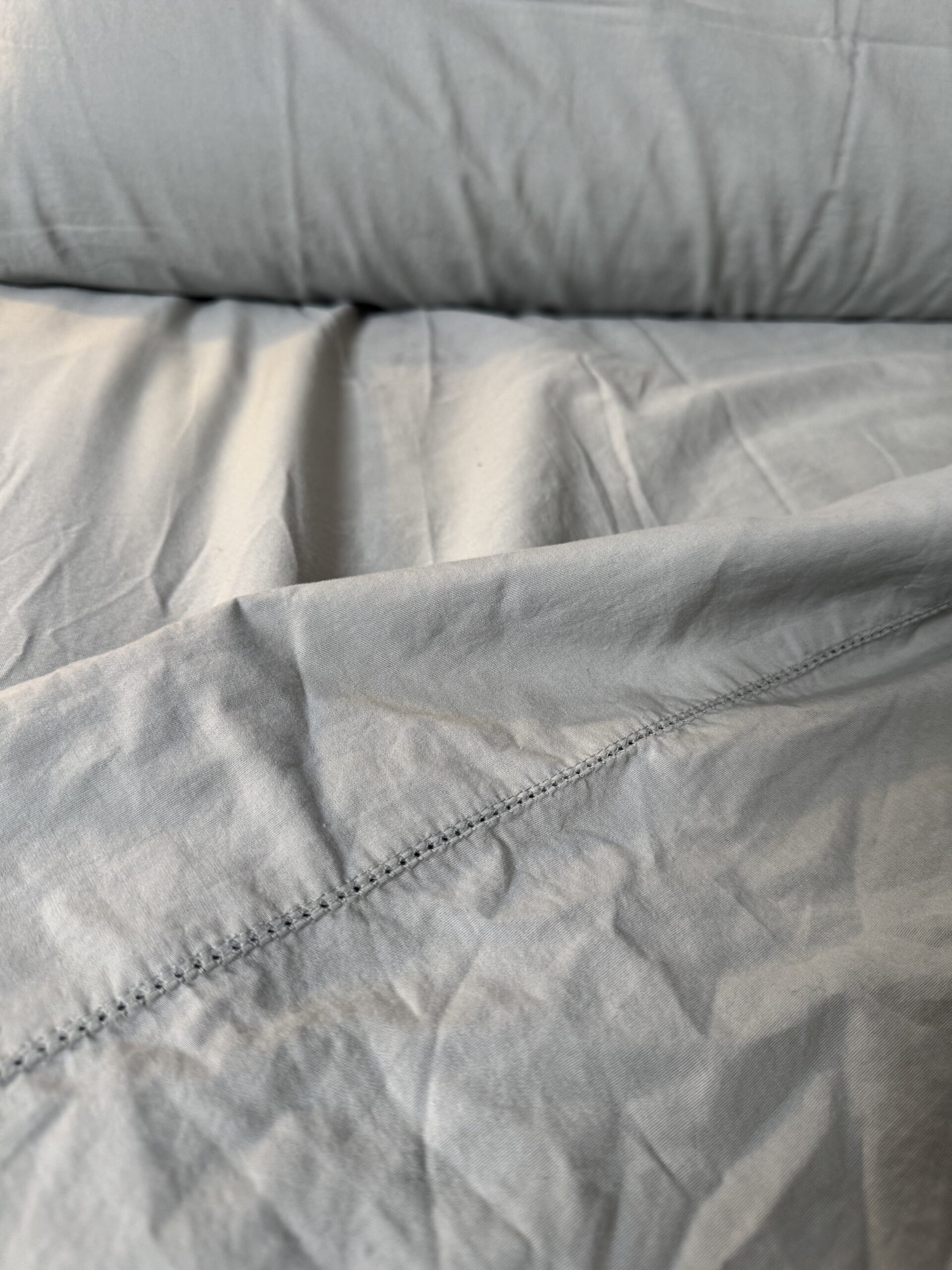 Close-up of a wrinkled gray bed sheet with visible stitching, folded over a mattress.