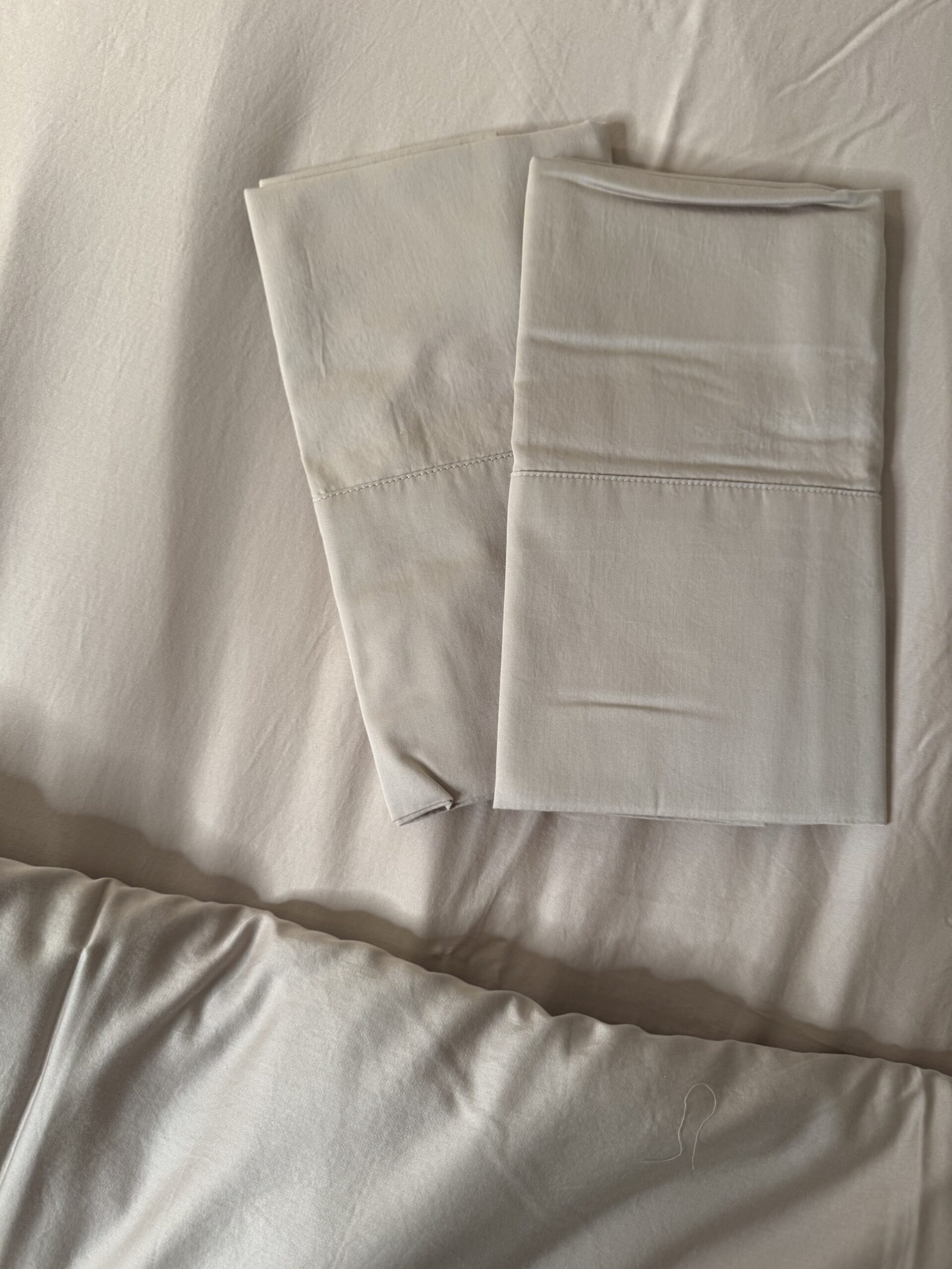 Two neatly folded white pillowcases are placed on a white bed sheet.