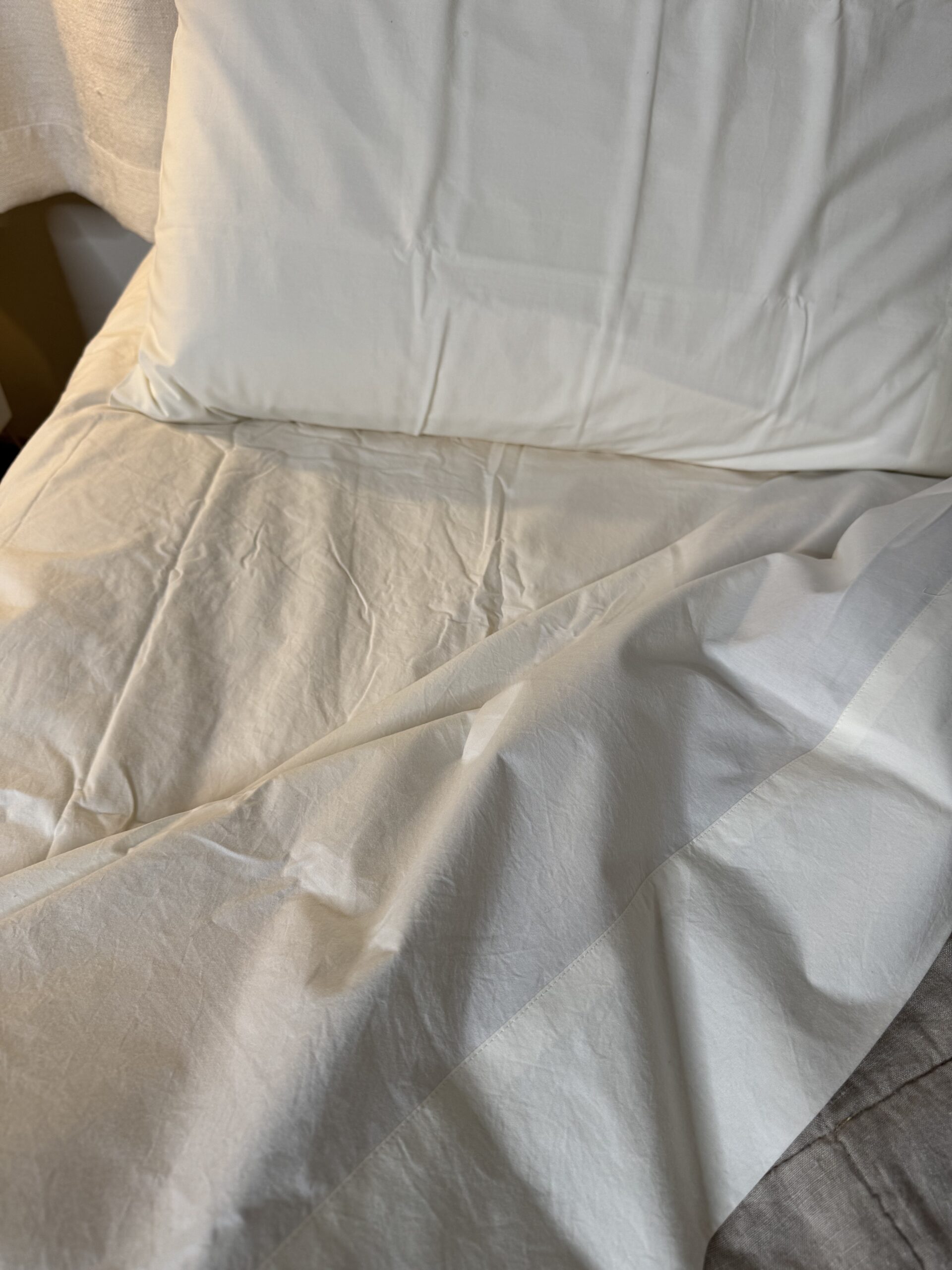 White bedsheet and pillow on a slightly wrinkled bed.