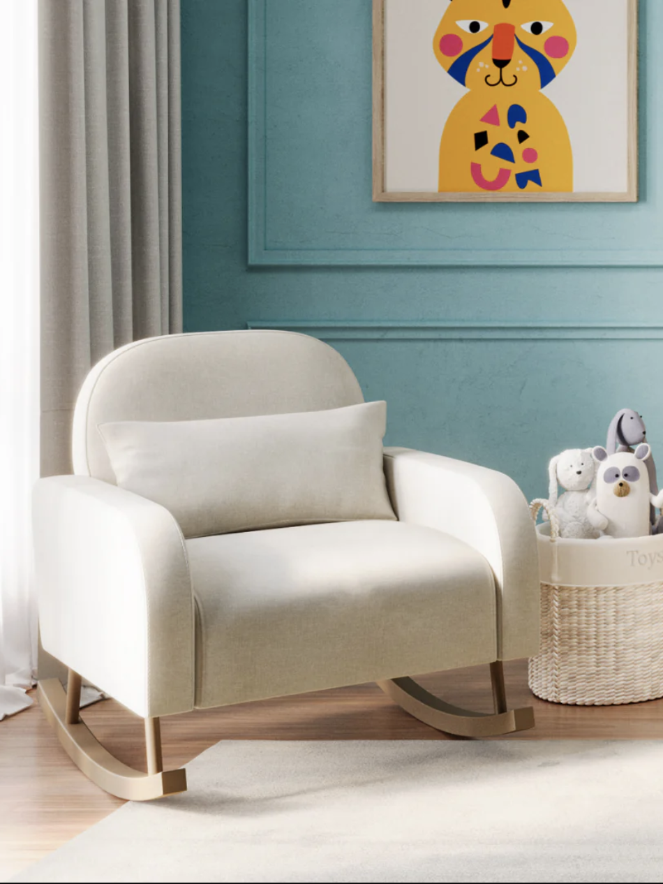 A beige rocking chair with a cushion is next to a basket of plush toys on the floor. A colorful animal print is on the teal wall in the background.