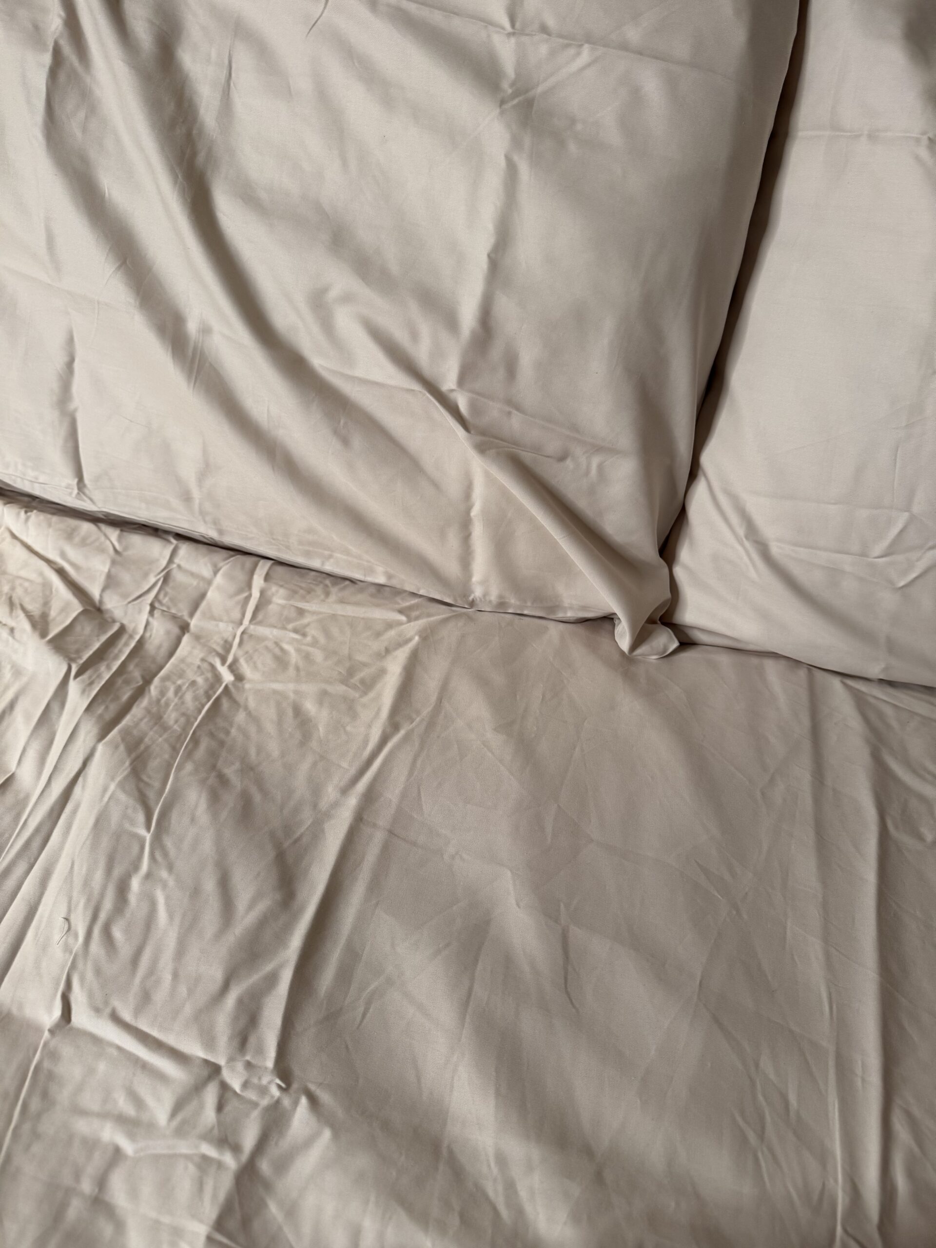 A wrinkled beige bedsheet with two matching pillowcases.