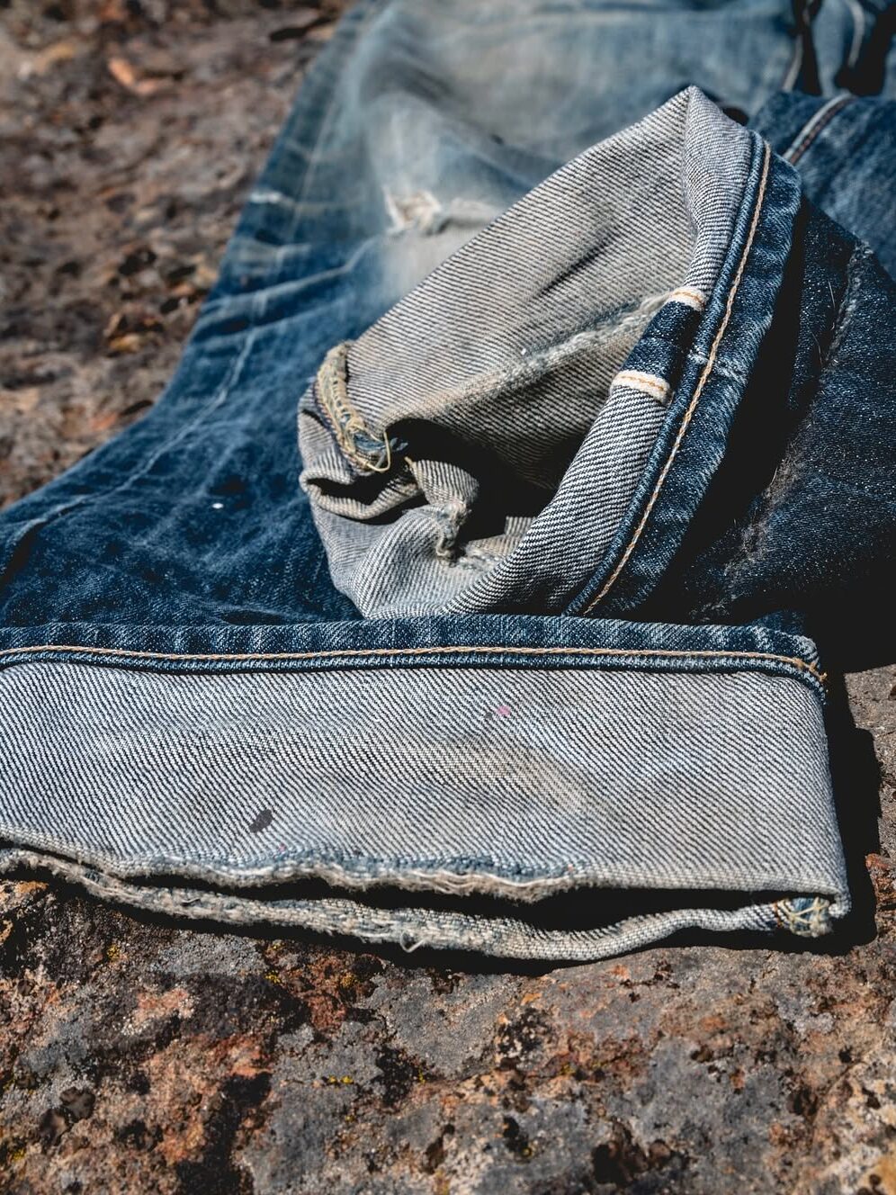 Close-up of a folded pair of denim jeans resting on a rocky surface.