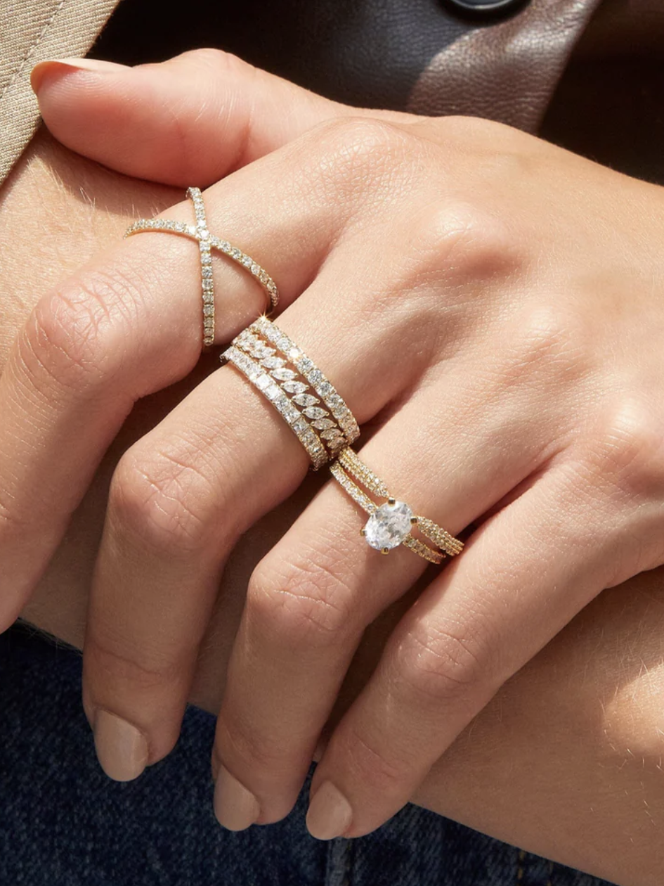 A hand displaying multiple gold rings with diamonds, including a crisscross design and a large solitaire.