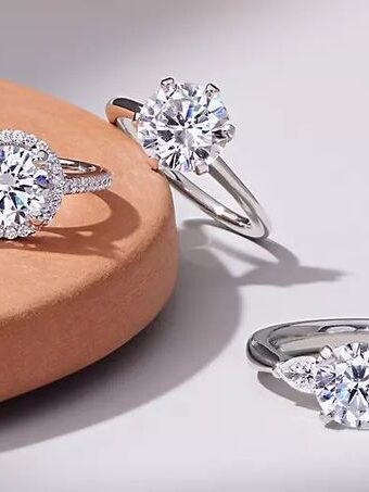 Three silver rings with large diamond-like stones displayed on a light brown and white surface.