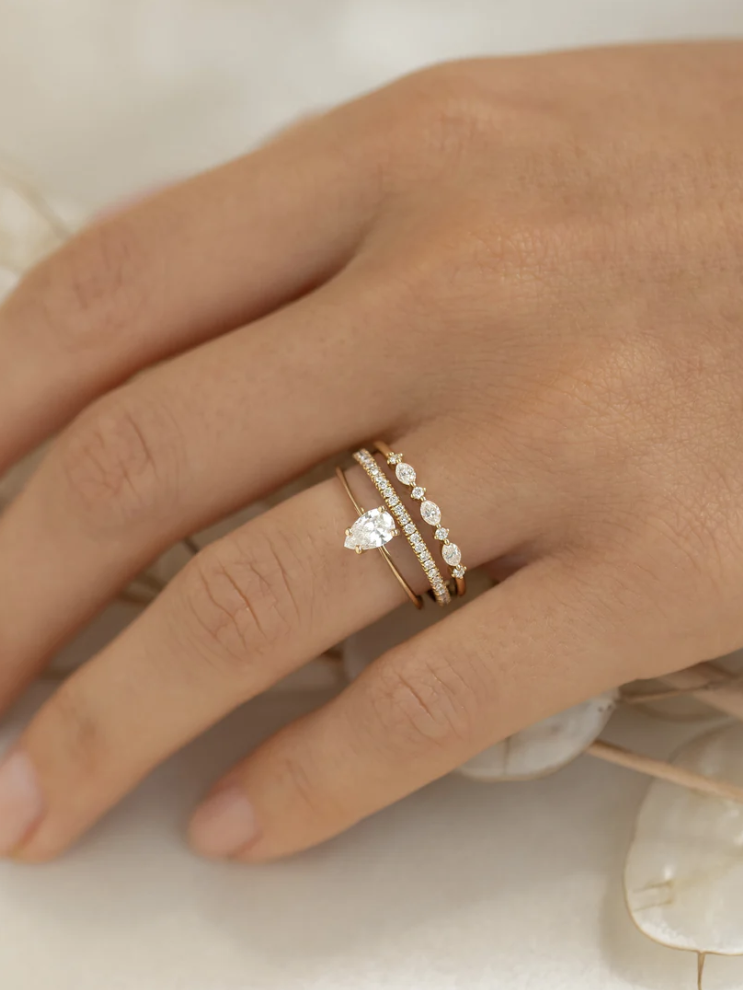 Close-up of a hand wearing two gold rings with diamonds on a light background.