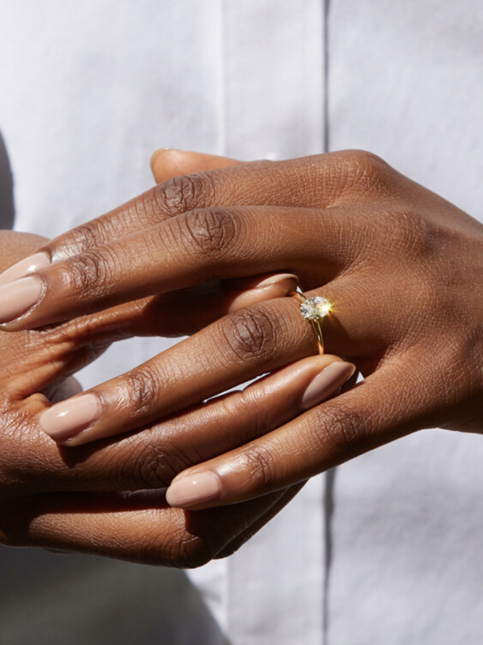 A person wearing a solitaire diamond ring holds their hands together against a white background.