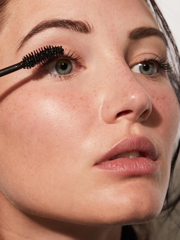 A person applies black mascara to their eyelashes with a brush wand.