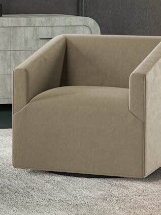 A beige armchair sits on a light gray carpet in front of a modern, gray chest of drawers.