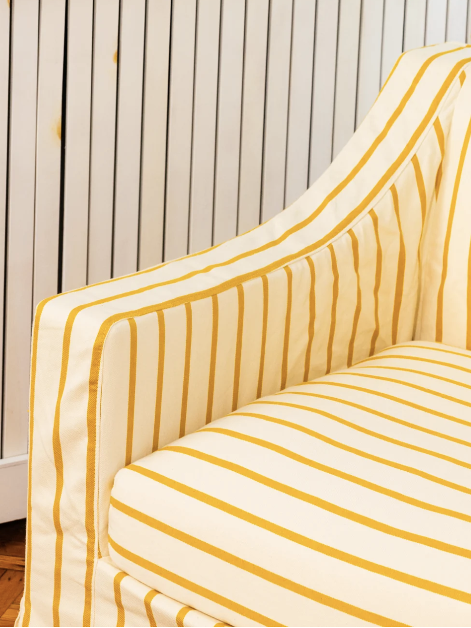 Close-up of a yellow and white striped armchair with a hardwood floor and white paneled background.