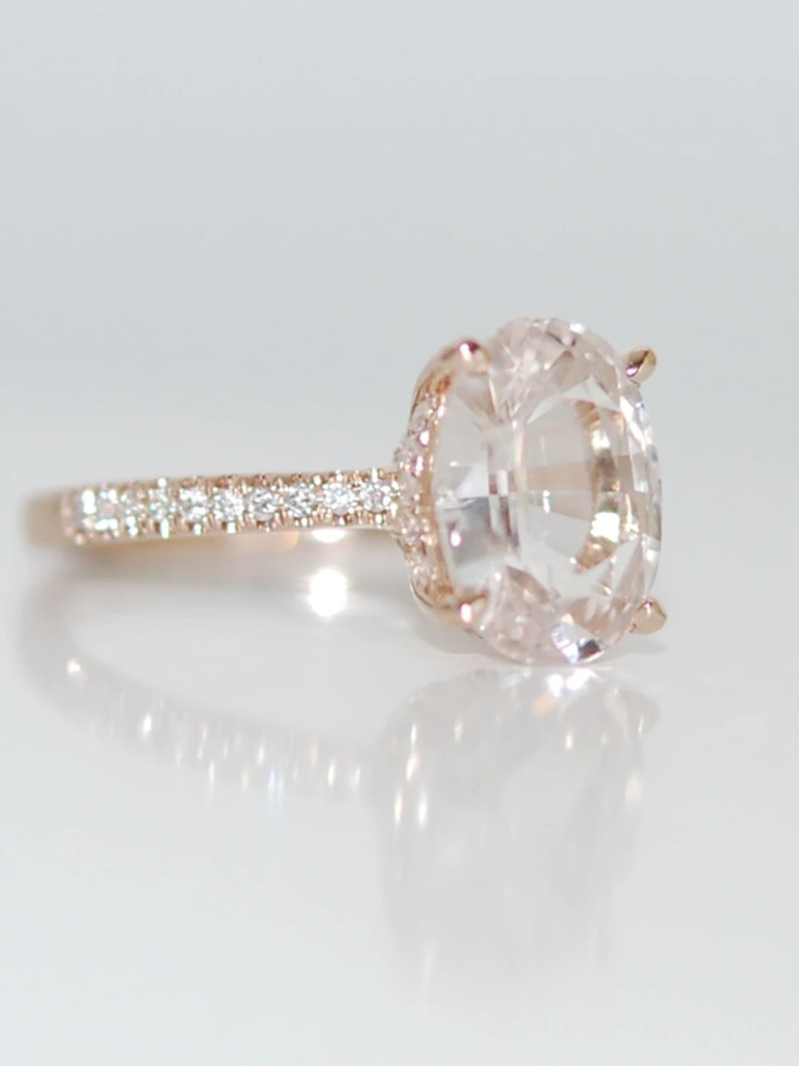 A rose gold ring with a large oval diamond at the center and a band adorned with small round diamonds.