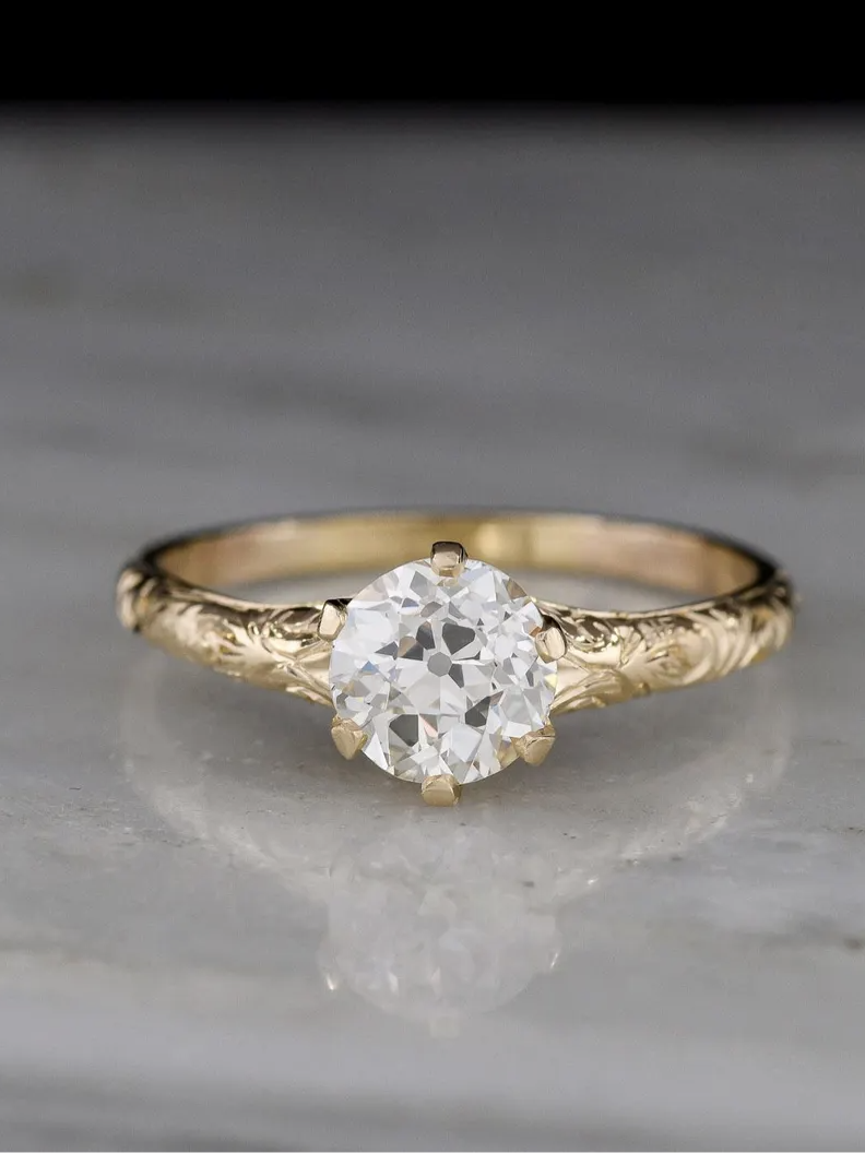 Gold ring with an intricate band design, featuring a round, clear gemstone set in a classic pronged setting.