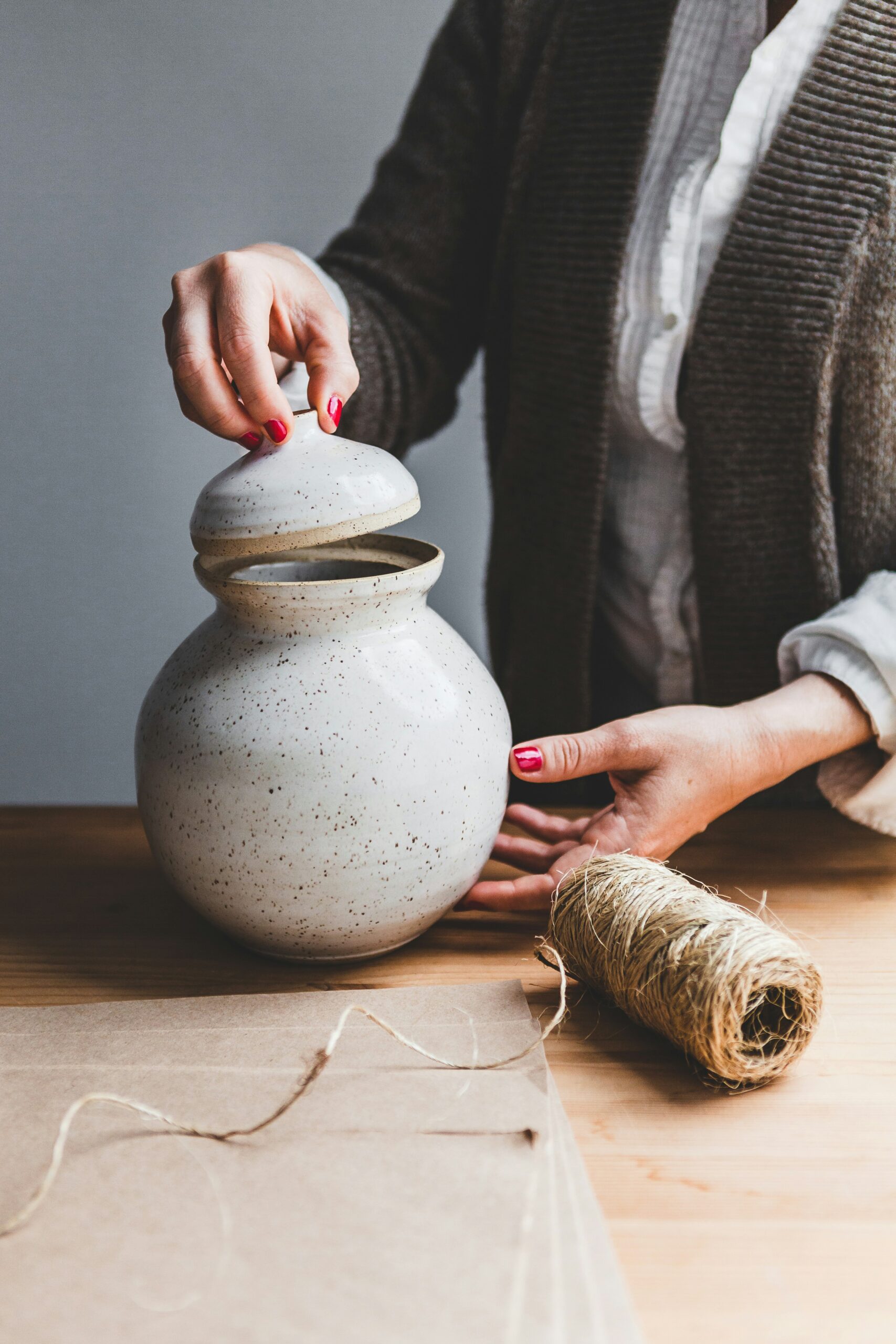 Person placing lid on a ceramic jar beside a spool of twine on a wooden table.