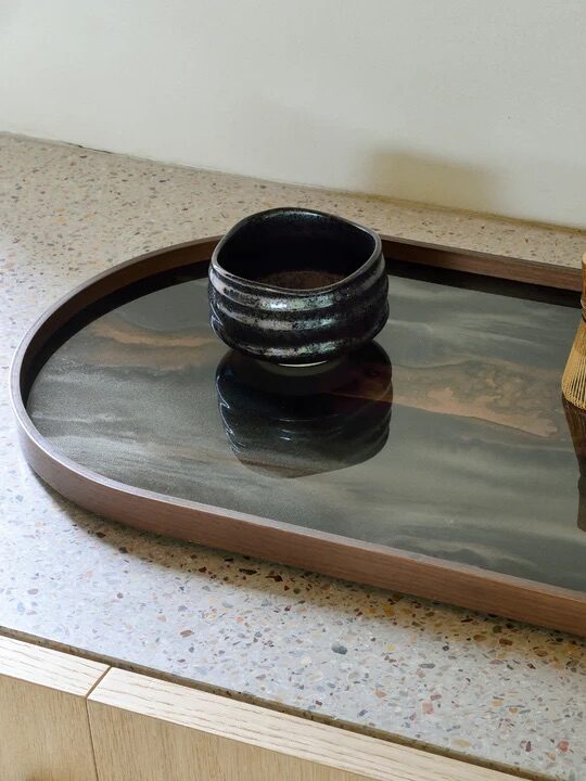 Ceramic bowl, bamboo whisk, and small vase on a wooden tray atop a speckled countertop.