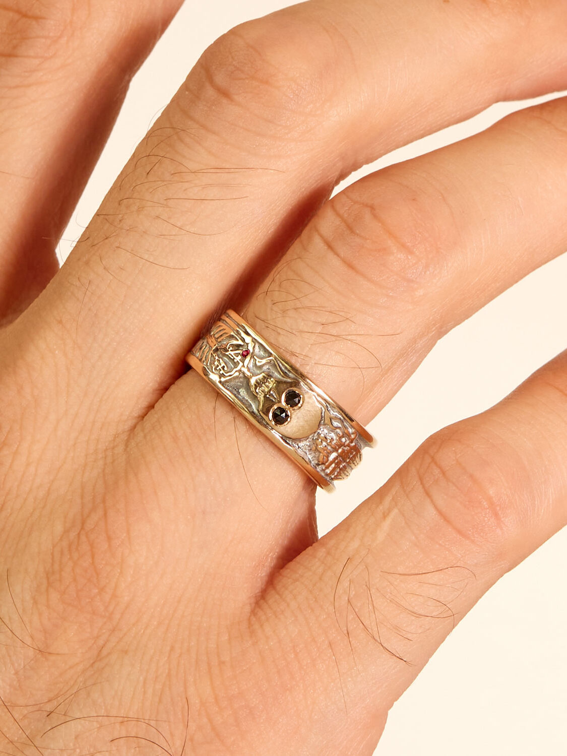 A hand wearing a silver ring with a small skull design, placed against a plain background.