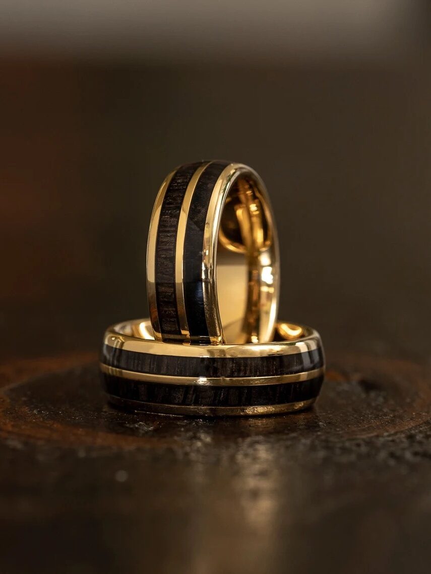 Two gold rings with black inlays, one standing upright and the other lying flat, on a dark wooden surface.