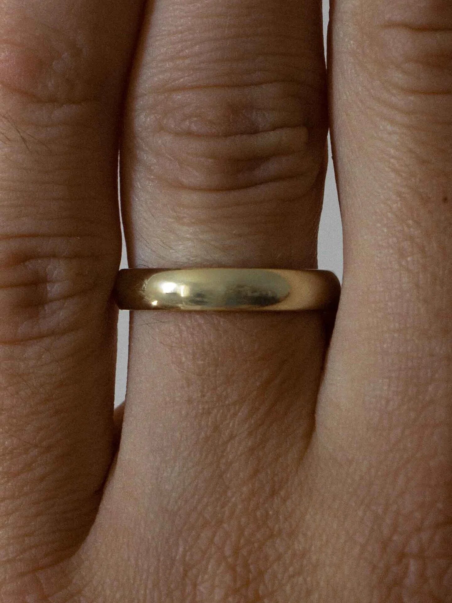 Close-up image of a person's hand wearing a simple, plain gold band on their ring finger.