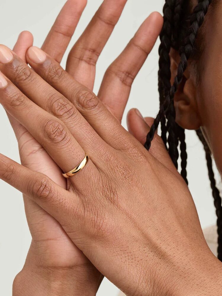 Person showing hands with a gold ring on a finger, braided hair visible, neutral background.