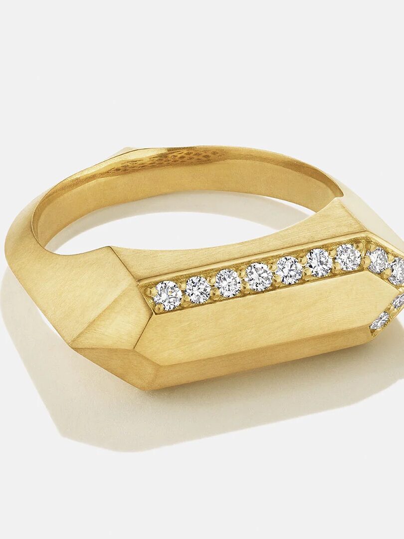 A gold ring with a geometric design featuring a row of small round diamonds across the top.