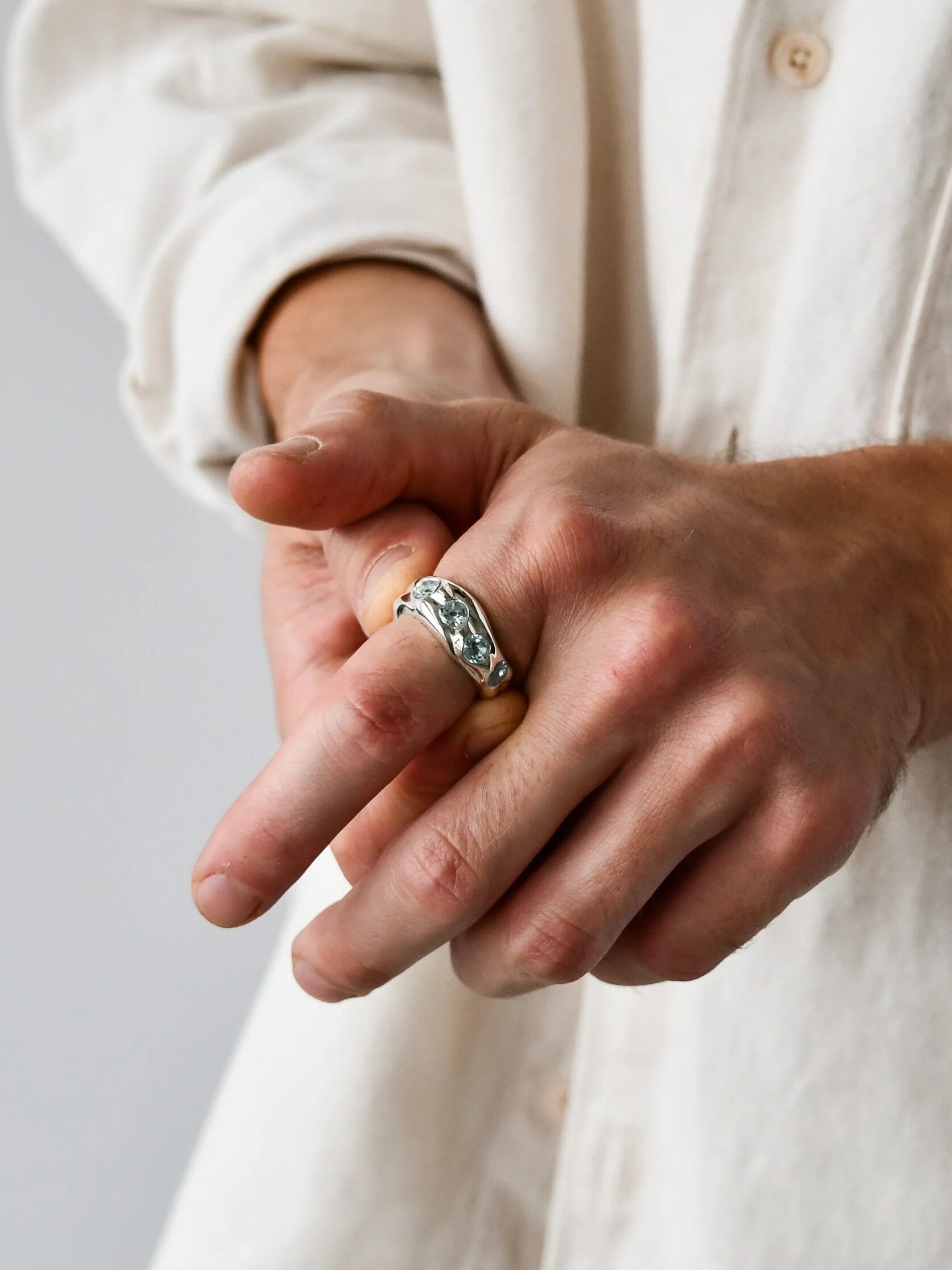 A person wearing a silver ring on their middle finger, adjusting it with the other hand. The person is wearing a cream-colored shirt.