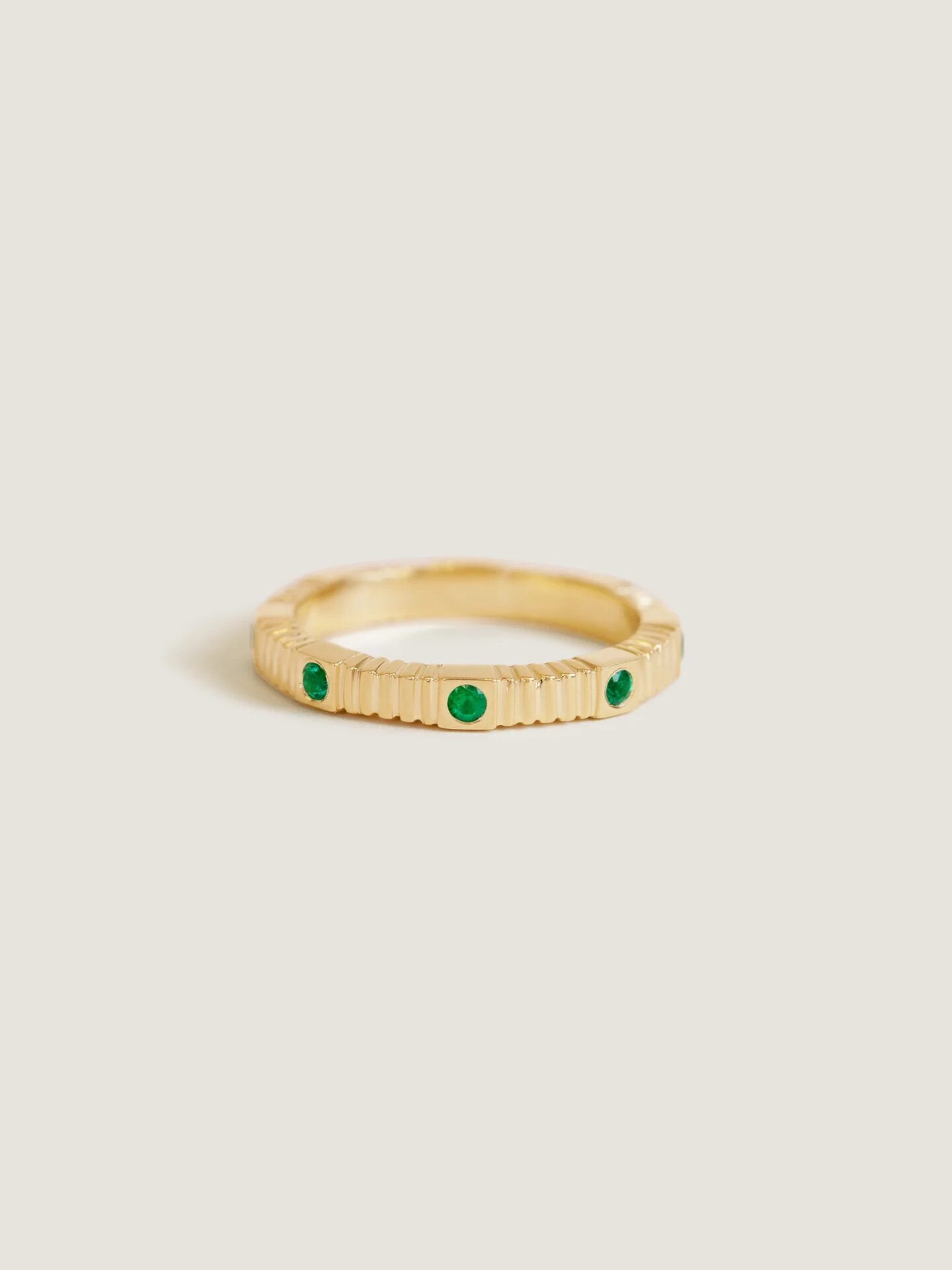 Gold ring with a textured band and three green gemstones evenly spaced around it, set against a plain background.