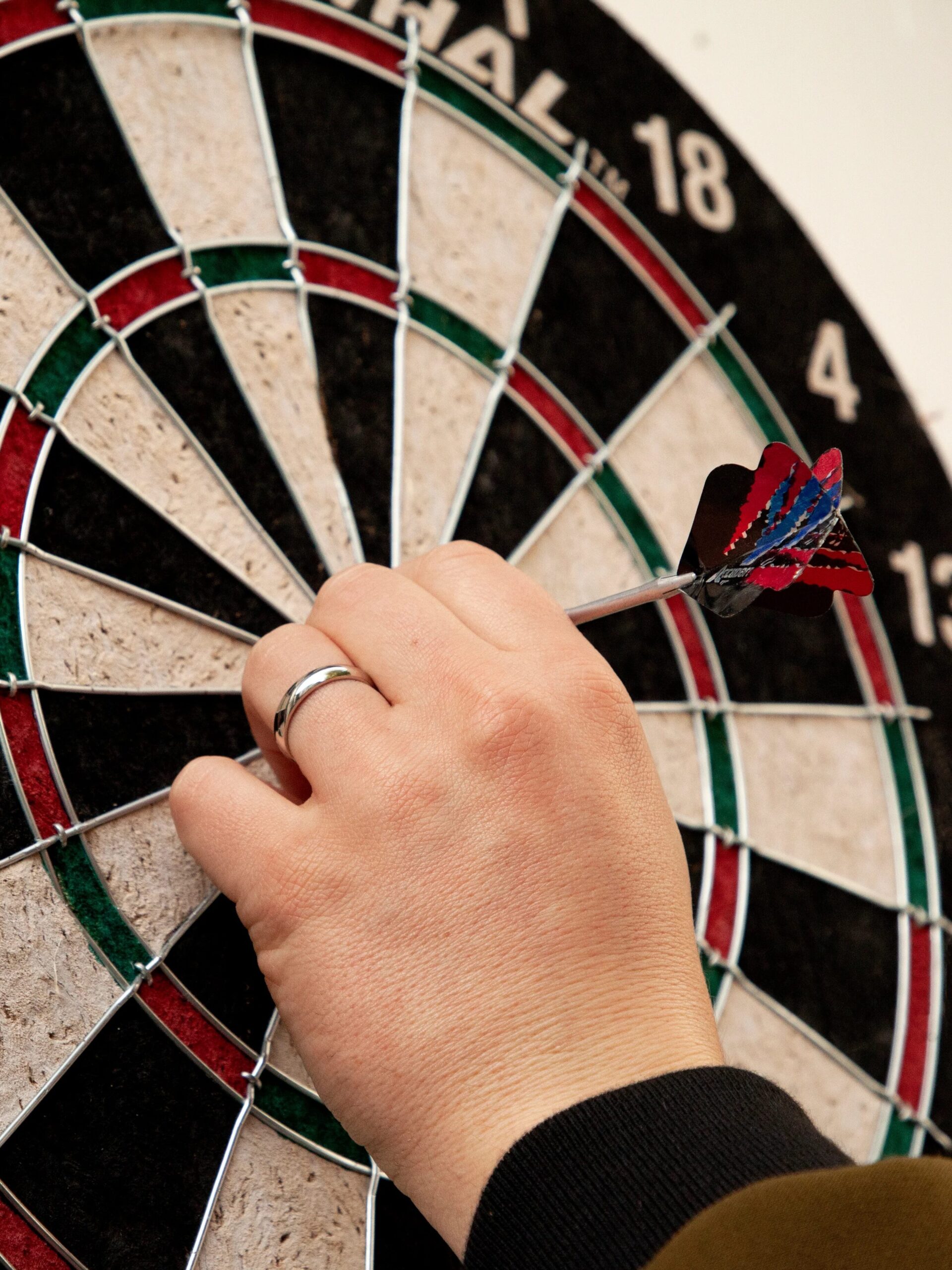 A hand wearing a ring pulls a dart from a dartboard.