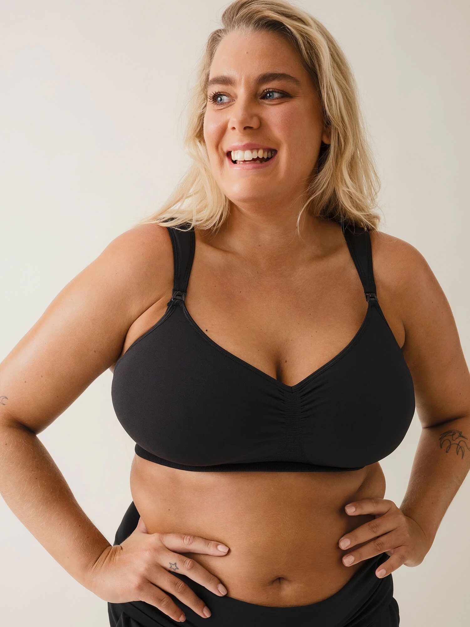 Woman smiling, wearing a black sports bra and black pants, standing against a plain background.