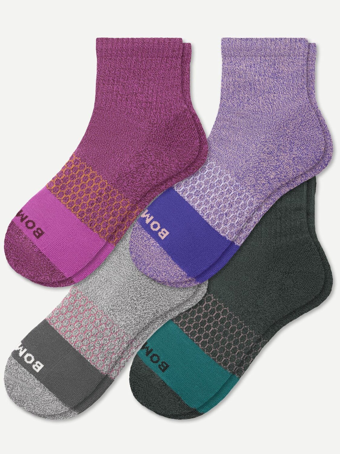 Four pairs of organic socks in shades of purple, pink, gray, and green, each featuring a textured design and labeled with "Bombas" on the sole.