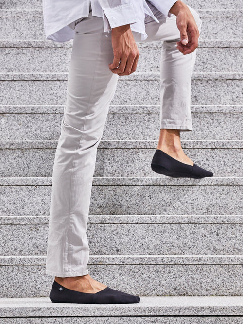 A person wearing black slip-on shoes and light pants, complemented by cozy organic socks, is walking up a set of gray concrete steps.