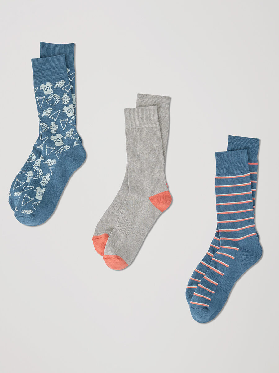 Three pairs of organic socks: one blue with white geometric patterns, one gray with orange heels and toes, and one blue with pink and orange stripes.