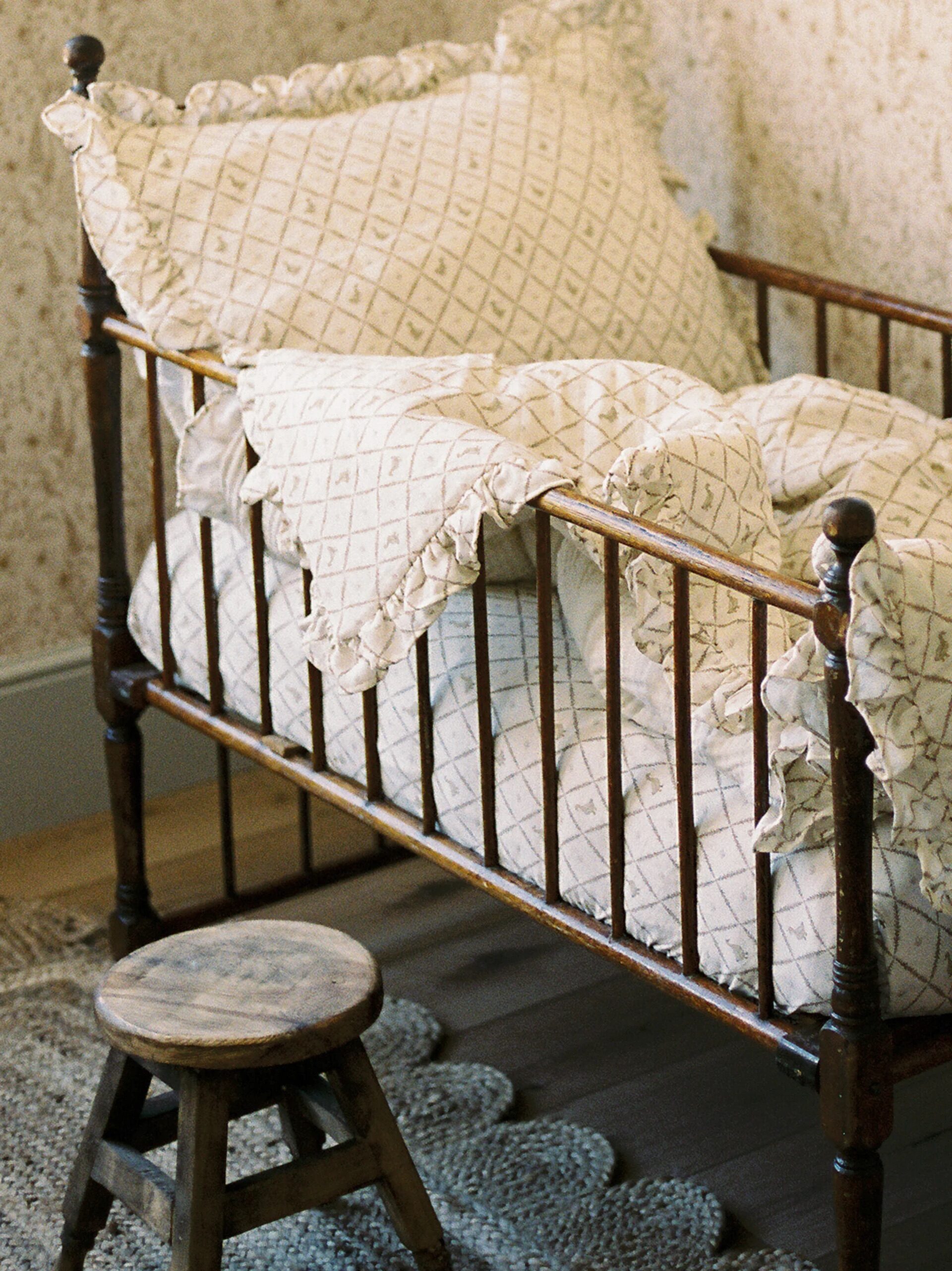 A vintage wooden bed with patterned bedding and a small wooden stool beside it on a textured rug.