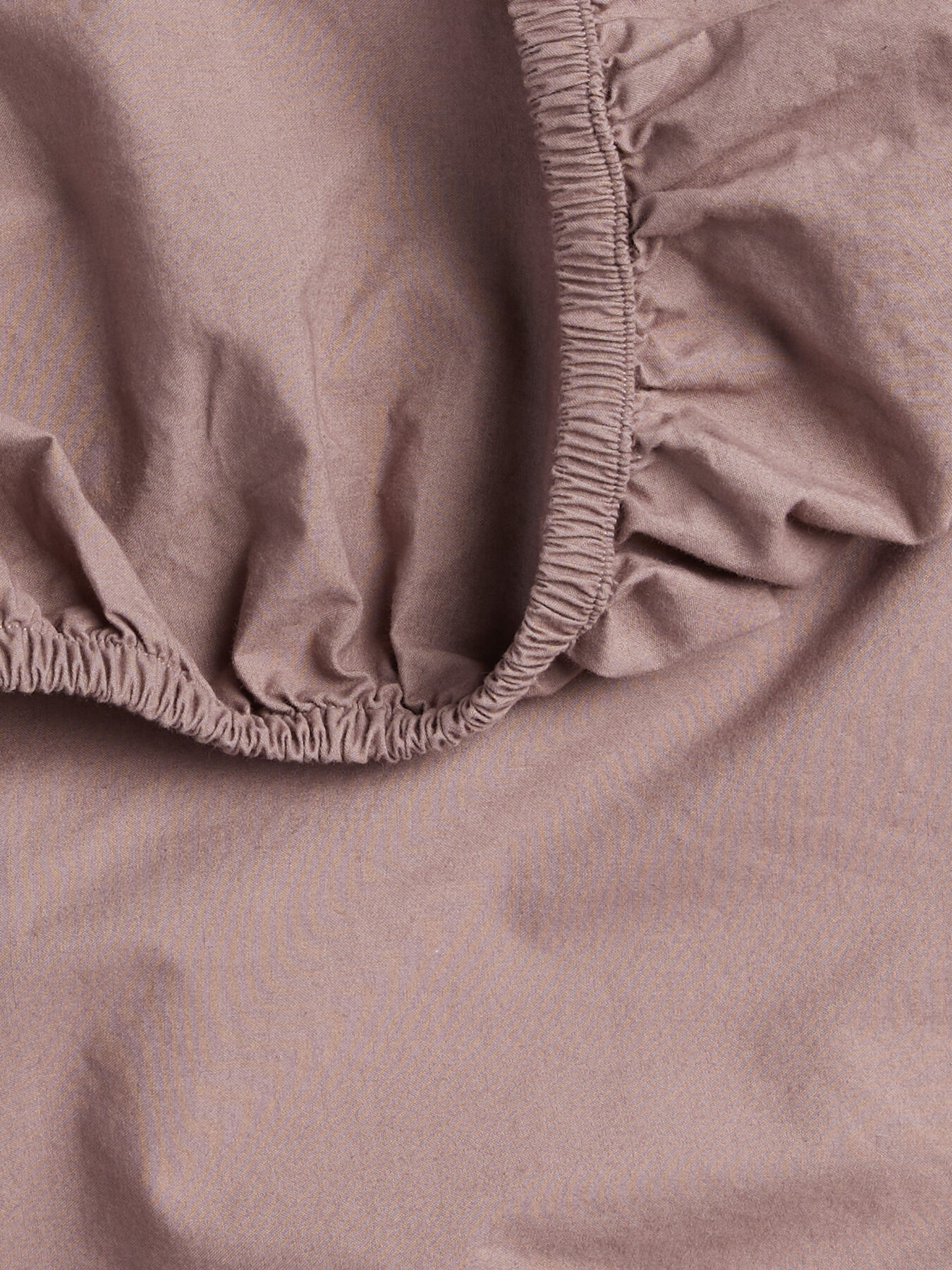 Close-up of a wrinkled light brown fabric with an elastic edge, resembling a fitted bed sheet.